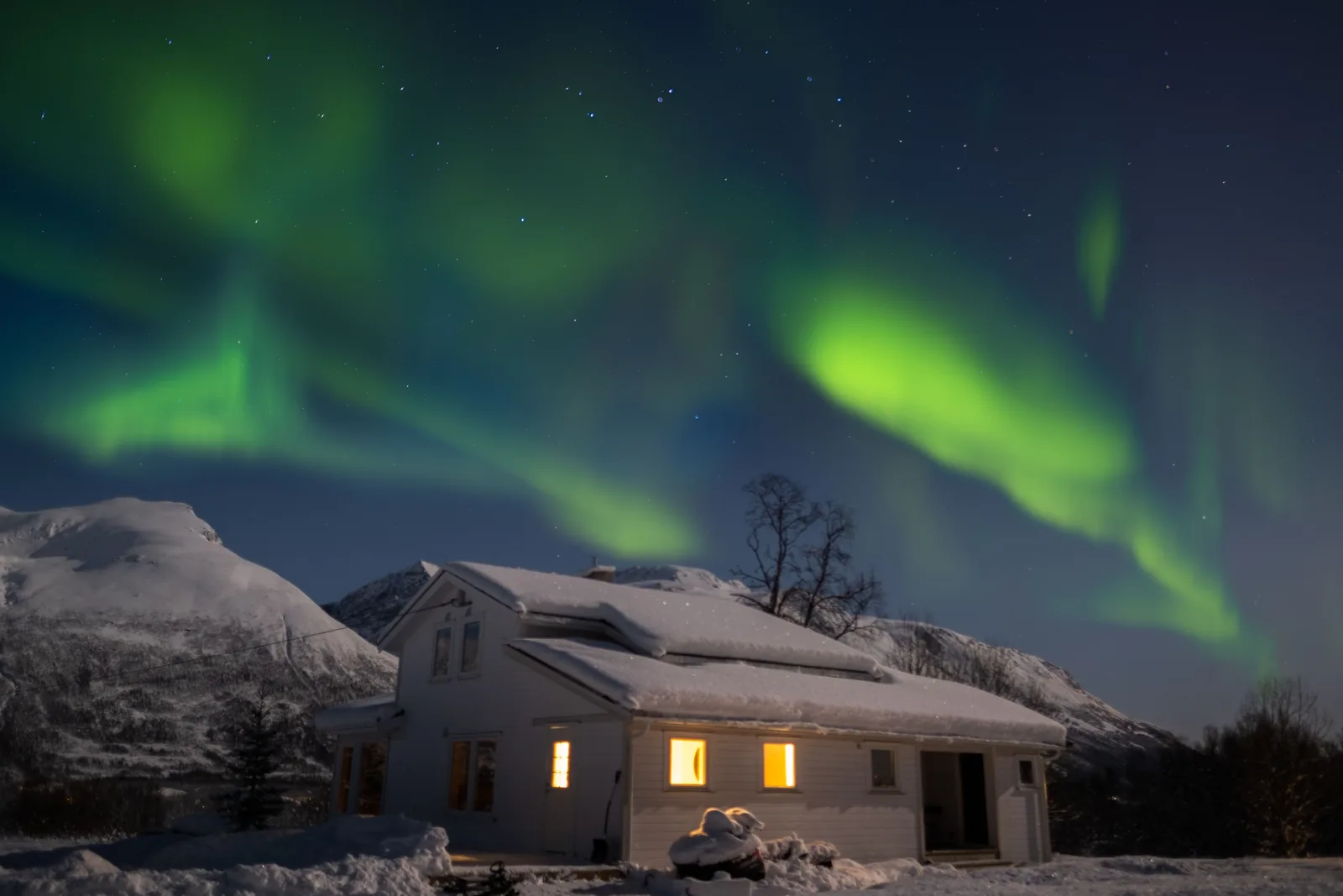 Aurora borealis over a snow-covered house and mountains near Tromsø, Norway