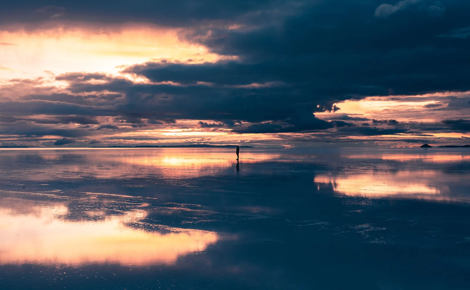 Lone person standing in the sunset reflection on the Uyuni salt flats, Bolivia