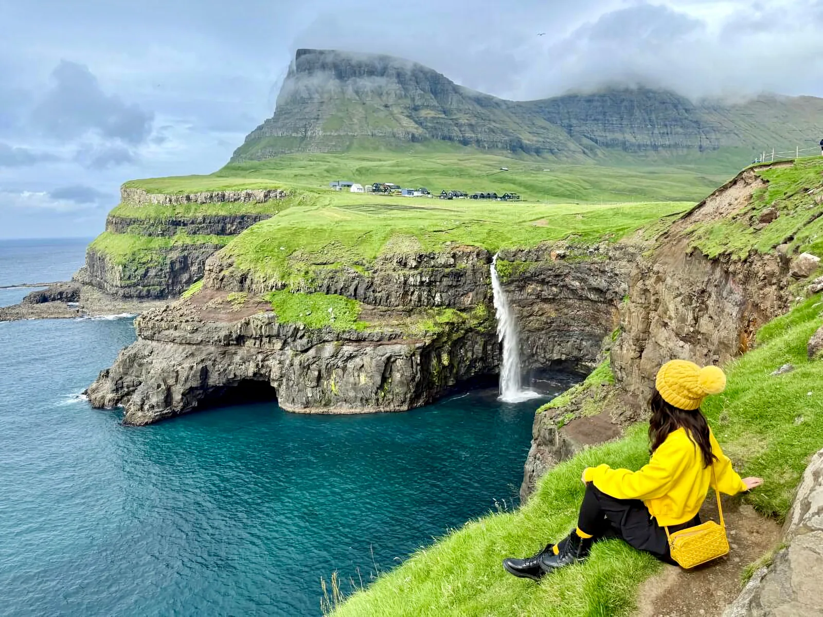 Traveller looking at Múlafossur waterfall falling into the ocean in the Faroe Islands