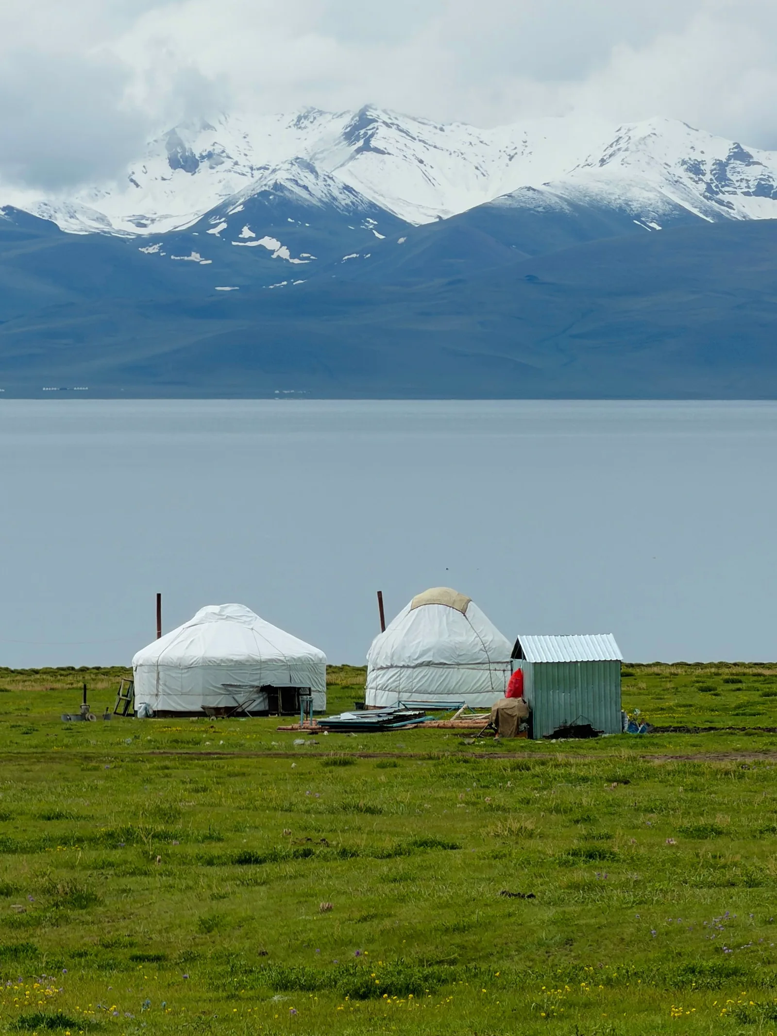 Traditional yurts beside a mountain lake with snow-capped peaks in Kyrgyzstan's Naryn Region