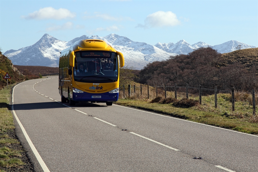 A Scottish Citylink coach driving through the Highlands with mountains in the background